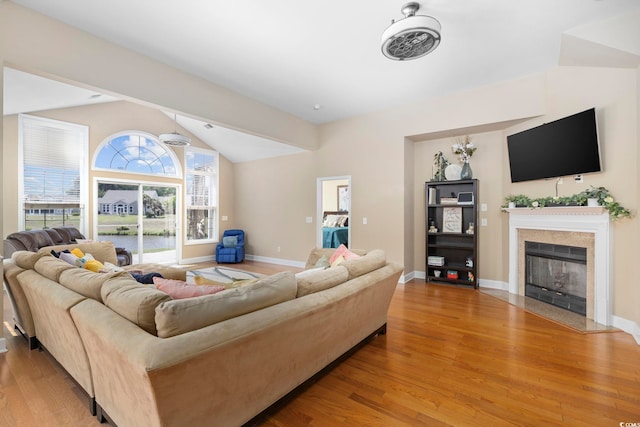 living room with baseboards, light wood-style floors, a fireplace with flush hearth, and vaulted ceiling