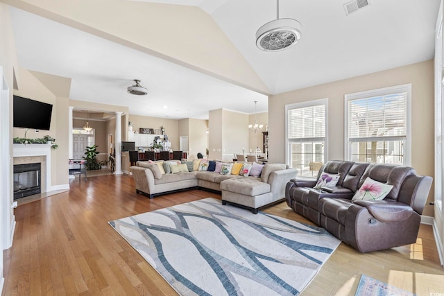 living area with light wood-style flooring, a glass covered fireplace, a notable chandelier, and visible vents