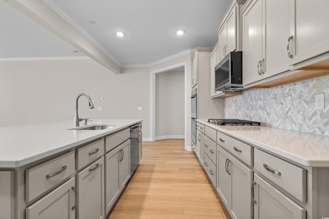 kitchen with a sink, appliances with stainless steel finishes, decorative backsplash, light wood-style floors, and light countertops