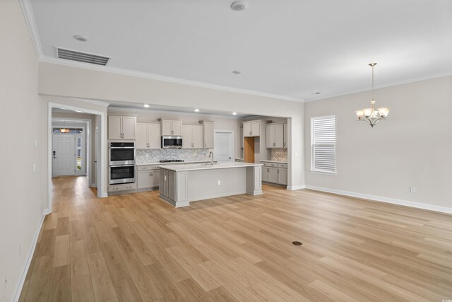kitchen with stainless steel appliances, backsplash, a chandelier, crown molding, and a center island with sink