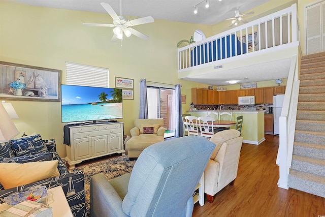 living room featuring ceiling fan, stairway, a towering ceiling, and dark wood-style flooring