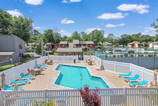 community pool with a patio, fence, and a residential view
