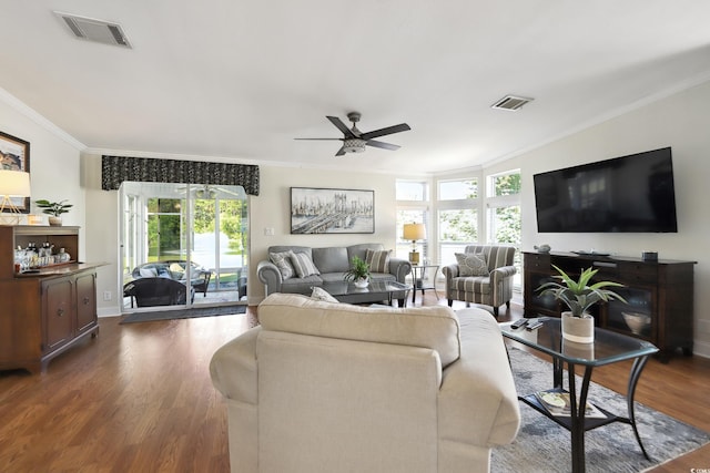 living area featuring crown molding, dark wood-style flooring, a ceiling fan, plenty of natural light, and baseboards