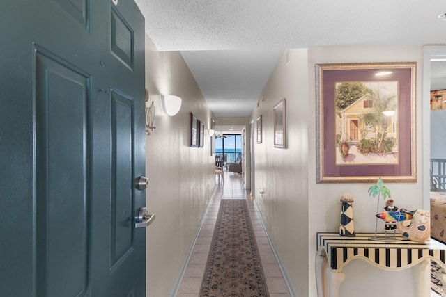 corridor with tile patterned floors, baseboards, and a textured ceiling