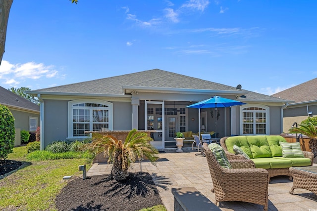 rear view of house featuring a patio area, stucco siding, a sunroom, outdoor lounge area, and roof with shingles