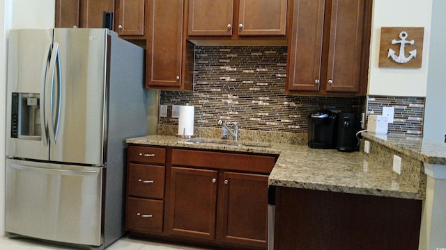 kitchen featuring stainless steel fridge with ice dispenser, a sink, decorative backsplash, and light stone countertops