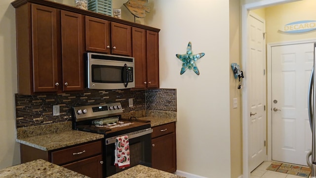 kitchen featuring stainless steel appliances, backsplash, light stone counters, and baseboards