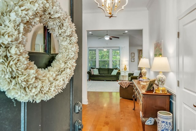 foyer with crown molding, a chandelier, light wood finished floors, and a ceiling fan