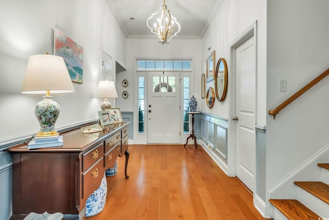 foyer entrance with stairs, light wood-style floors, a chandelier, a decorative wall, and crown molding