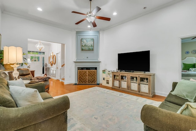 living area with wood finished floors, recessed lighting, ornamental molding, ceiling fan, and a chandelier