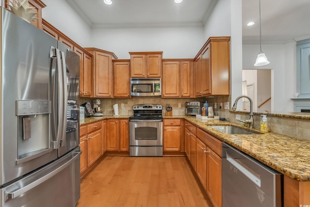 kitchen with stainless steel appliances, a sink, crown molding, light wood-style floors, and brown cabinetry