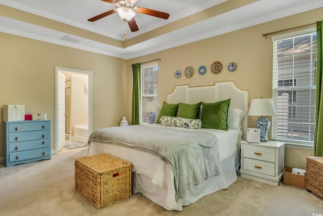bedroom featuring light carpet, crown molding, a tray ceiling, ensuite bath, and ceiling fan