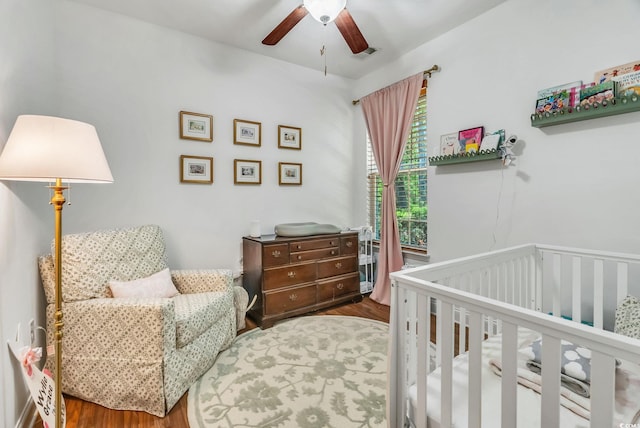 bedroom featuring wood finished floors, a nursery area, and ceiling fan