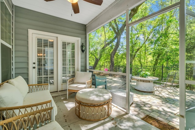 sunroom with a ceiling fan, an outdoor living space with a fire pit, and view of wooded area