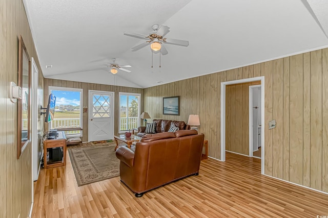 living area with light wood finished floors, a ceiling fan, lofted ceiling, and wood walls