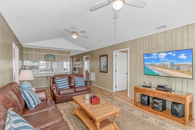 living room featuring ceiling fan, light wood finished floors, wood walls, and lofted ceiling