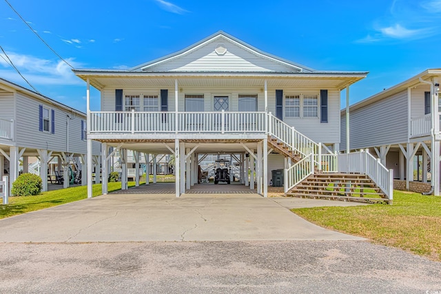 coastal home with covered porch, a carport, driveway, stairs, and a front yard