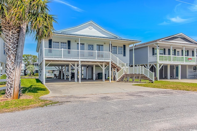 raised beach house featuring a porch, concrete driveway, a carport, and stairway