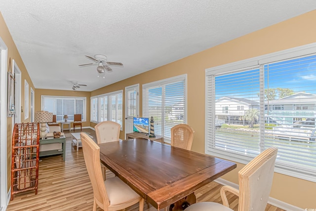 dining space featuring light wood finished floors, a textured ceiling, ceiling fan, and baseboards