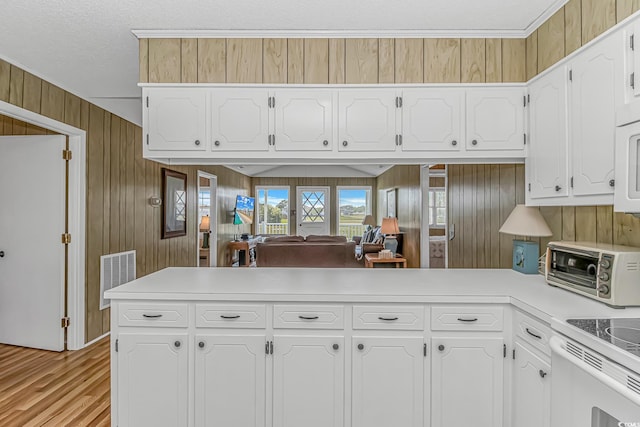 kitchen featuring a peninsula, white cabinets, light countertops, light wood-style floors, and wood walls