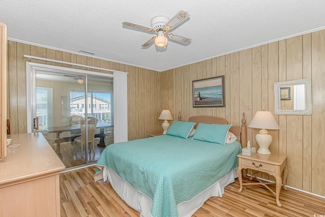 bedroom with light wood-style flooring, ornamental molding, wood walls, a textured ceiling, and access to exterior