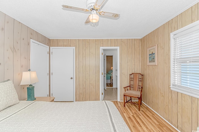 bedroom featuring ornamental molding, light wood-type flooring, a textured ceiling, wooden walls, and a ceiling fan