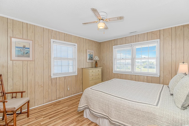 bedroom featuring wood finished floors, ornamental molding, baseboards, wood walls, and ceiling fan