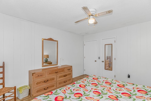 bedroom with ceiling fan, a textured ceiling, and a decorative wall