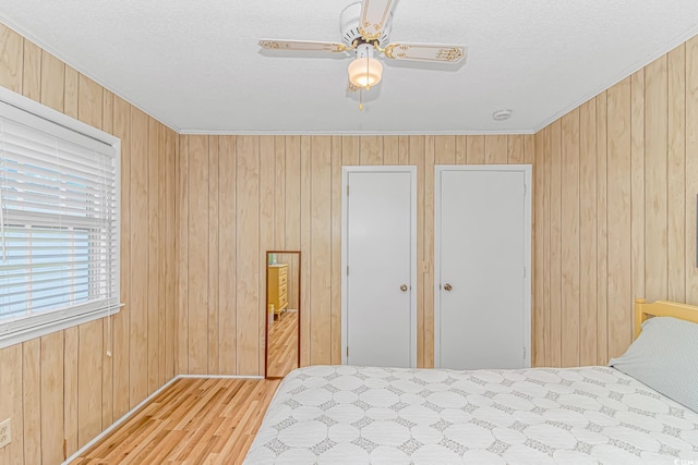 bedroom featuring wood finished floors, wood walls, crown molding, a textured ceiling, and baseboards