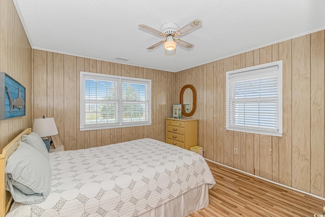bedroom featuring wood finished floors, baseboards, crown molding, wood walls, and a ceiling fan