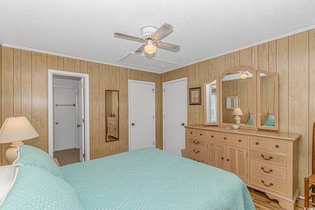 bedroom with ornamental molding, wood walls, attic access, a textured ceiling, and ceiling fan