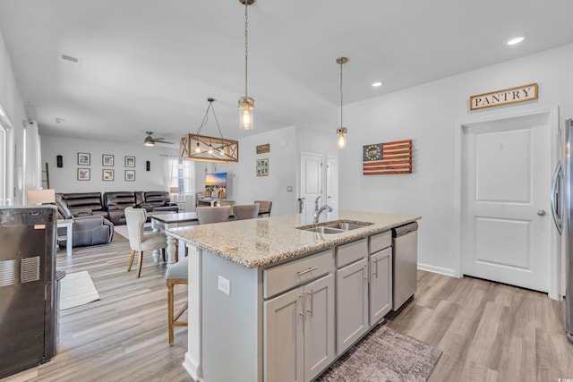 kitchen with a sink, appliances with stainless steel finishes, light wood-style floors, ceiling fan, and light stone counters
