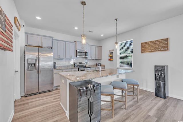 kitchen featuring stainless steel appliances, light wood finished floors, gray cabinets, a kitchen bar, and a sink