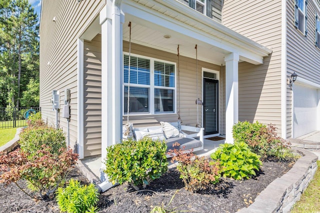 view of exterior entry featuring covered porch, fence, and a garage