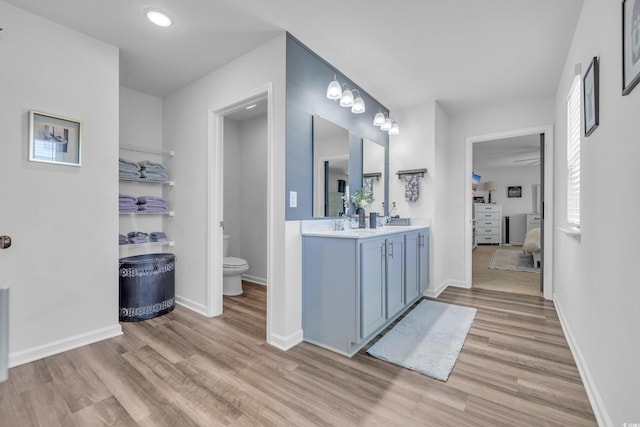 bathroom featuring wood finished floors, toilet, ensuite bathroom, double vanity, and recessed lighting