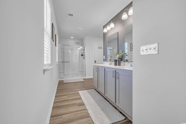 full bathroom featuring a shower stall, wood finished floors, double vanity, and baseboards