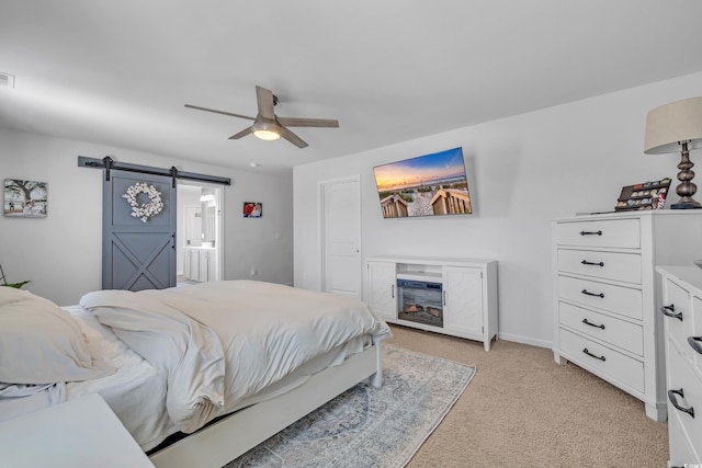 bedroom with light carpet, a barn door, ceiling fan, ensuite bathroom, and baseboards