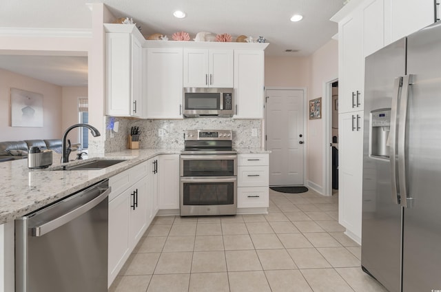 kitchen with stainless steel appliances, a sink, white cabinetry, tasteful backsplash, and crown molding