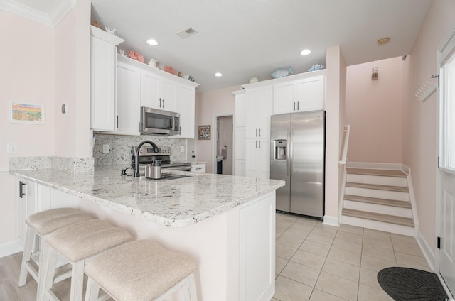 kitchen featuring appliances with stainless steel finishes, a peninsula, light stone counters, a kitchen bar, and white cabinetry