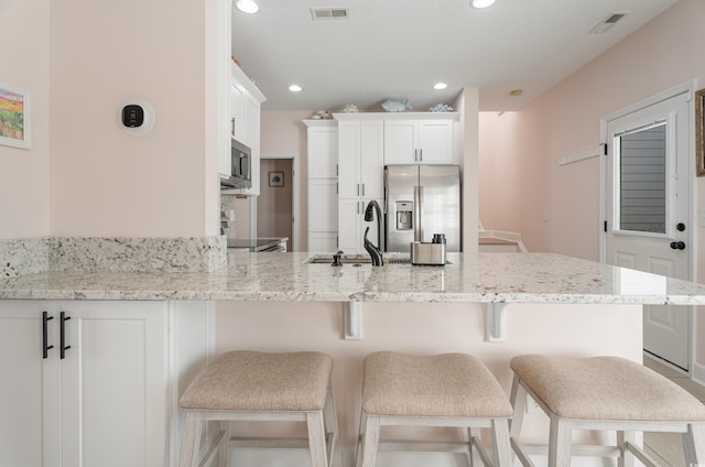 kitchen with appliances with stainless steel finishes, a sink, a peninsula, white cabinets, and light stone countertops