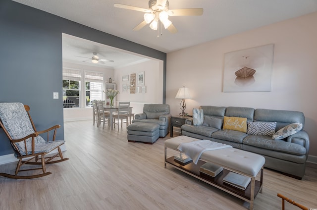 living area with light wood finished floors, a ceiling fan, baseboards, and crown molding