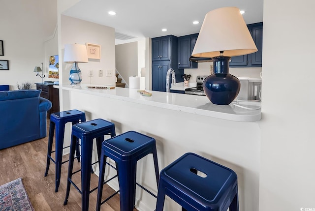 kitchen featuring stainless steel electric stove, wood finished floors, a sink, a kitchen breakfast bar, and light countertops