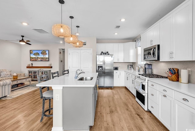 kitchen with stainless steel appliances, a sink, a kitchen breakfast bar, light wood-style flooring, and recessed lighting