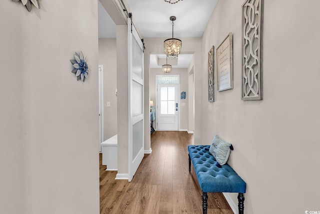 corridor featuring wood-type flooring, a barn door, and baseboards