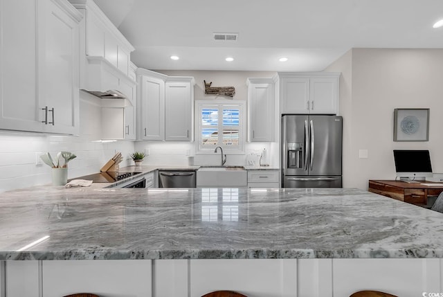 kitchen with stainless steel appliances, a sink, light stone counters, white cabinetry, and recessed lighting