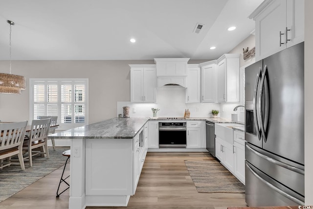 kitchen featuring appliances with stainless steel finishes, a peninsula, light stone countertops, white cabinetry, and light wood-type flooring