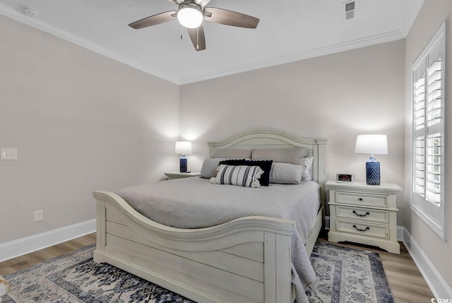 bedroom with multiple windows, light wood-style floors, ornamental molding, baseboards, and a ceiling fan
