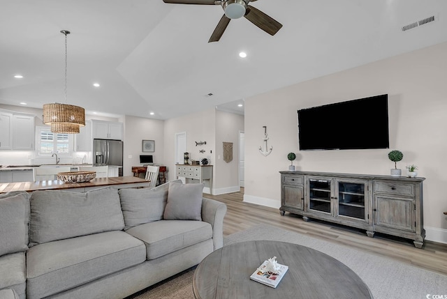 living area featuring light wood finished floors, a ceiling fan, vaulted ceiling, baseboards, and recessed lighting