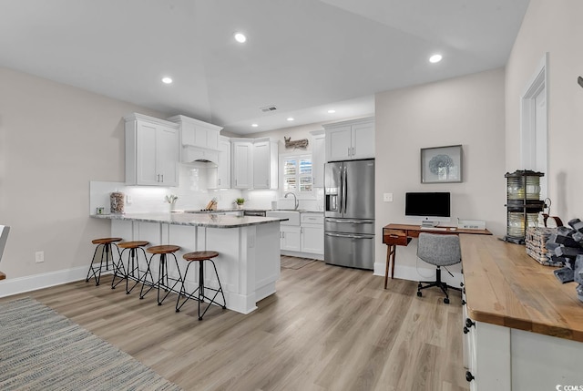 kitchen with stainless steel refrigerator with ice dispenser, a peninsula, a sink, light wood-style flooring, and white cabinetry