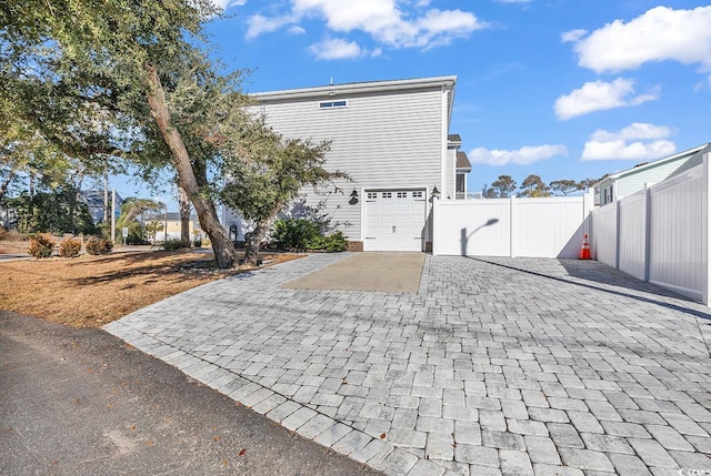view of property exterior with decorative driveway, an attached garage, and fence
